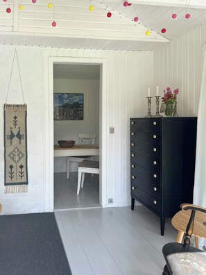 A room with a white wall, a black dresser, a wooden chair, and a table with a painting. - Cosy cabin collection in Veddinge Bakker (Asnæs)