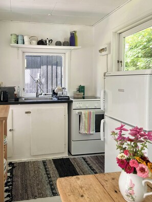 Ett kompakt kök med ett fönster, en ugn från Siemens, ett kylskåp och ett träbord med en vas med blommor.