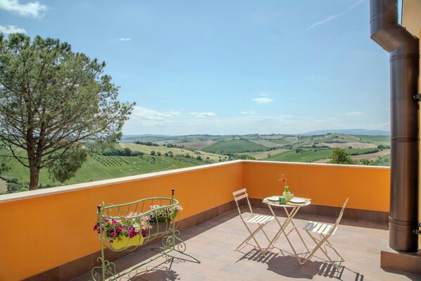 A balcony with a table, chairs, a metal chair with flowers, and a view of rolling hills. - Flat with views in Belvedere (Belvedere Ostrense)