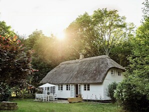 Une maison à toit de chaume, aux murs blancs, entourée d’une végétation luxuriante.