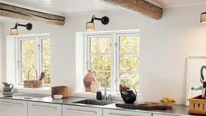 A modern kitchen with white cabinets, a black countertop, a window with a view of greenery, and a wooden ceiling beam.