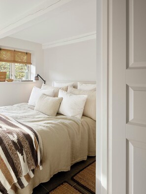 Une chambre à coucher avec un lit, des oreillers, une lampe de chevet, une fenêtre donnant sur un paysage agréable et une porte.