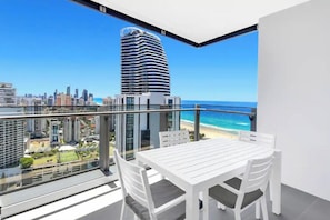 Ein Balkon mit Tisch und Stühlen mit Blick auf Strand und Stadtlandschaft.
