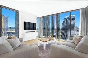Ein modernes Wohnzimmer mit Flachbildfernseher, zwei Sofas, einem Couchtisch und großen Fenstern mit Blick auf die Stadt.