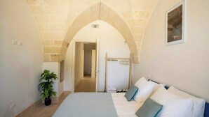 Un dormitorio con una cama, una planta en maceta, un perchero y un pasillo que da a otra habitación.