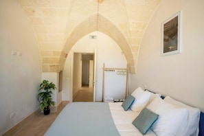 Ein Schlafzimmer mit einem Bett, einer Zimmerpflanze, einem Kleiderständer und einem Flur, der in einen anderen Raum führt.
