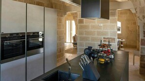 Una cocina moderna con paredes de piedra, electrodomésticos integrados y una isla central con fregadero y utensilios.