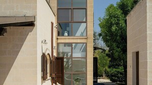 Un edificio moderno con fachada de vidrio, sillones de exterior y cielo despejado.