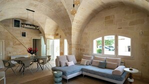 Una habitación amplia con techo de piedra, un sofá modular, una mesa de comedor con sillas y un ventanal grande.