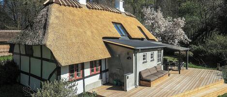 Een traditioneel rieten huis met een houten terras en een klein zitgedeelte buiten.