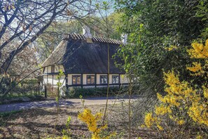 Ein traditionelles Haus mit Strohdach, umgeben von Bäumen und einem Garten.
