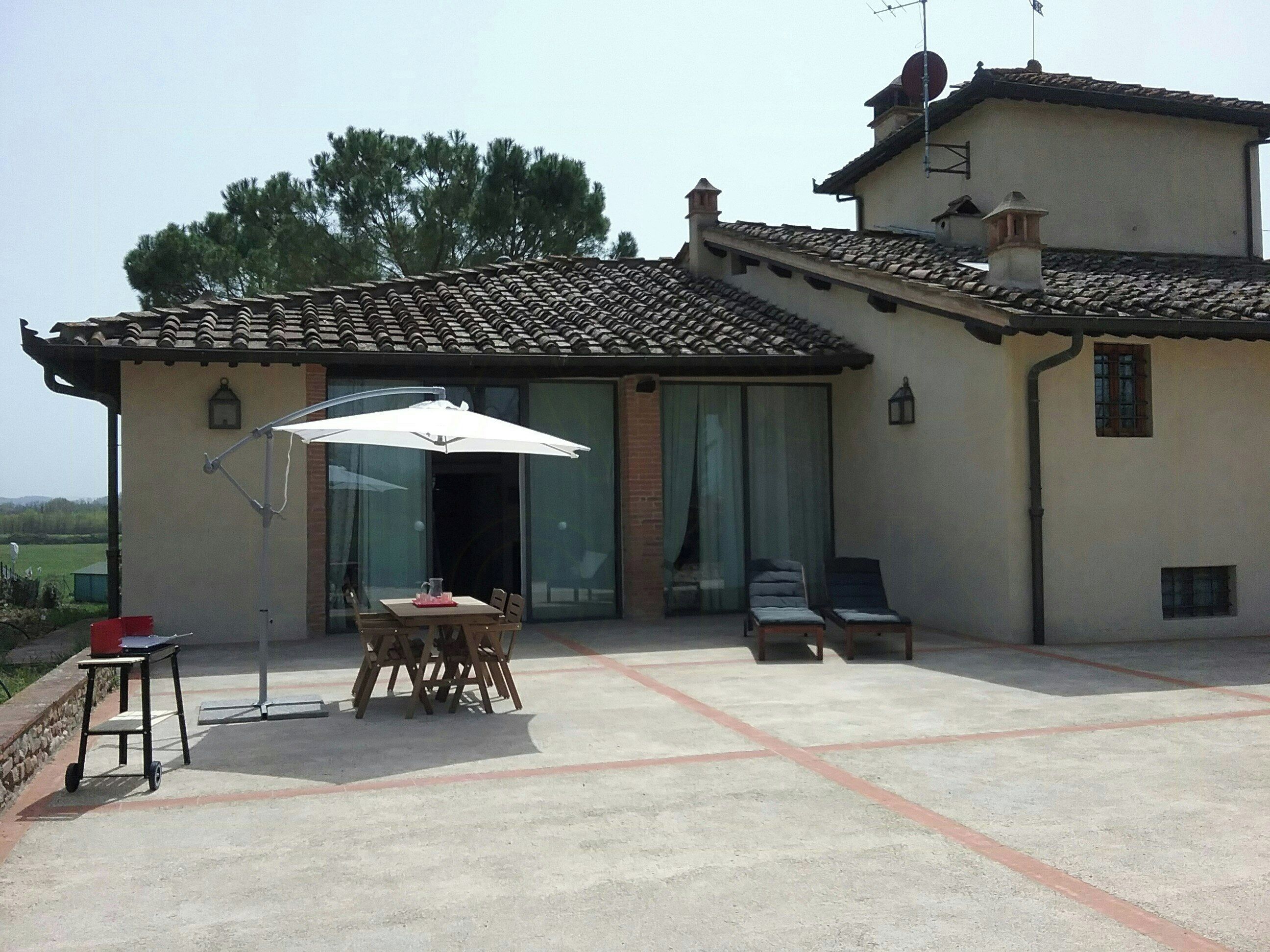 Una casa con un patio, una mesa y sillas, y una sombrilla grande.
