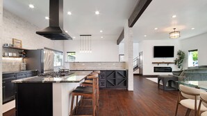 A modern kitchen with a large island, dark wood flooring, and a built-in TV.