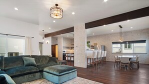 A spacious living area with a sectional sofa, a dining table with chairs, and a kitchen in the background.