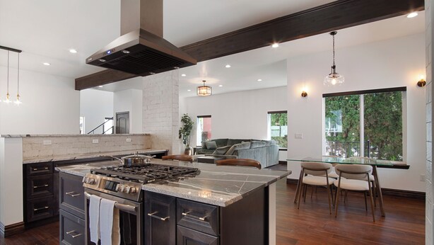 A modern kitchen with a large island, dark wood flooring, and a view to the living area.