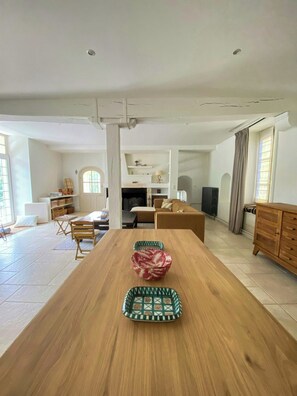 Ein geräumiger Wohnbereich mit Esstisch aus Holz, einer Couch und einem Fernseher.