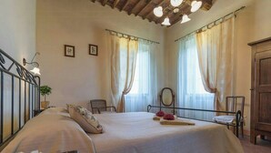 Un dormitorio con una cama, dos sillas, un armario de madera y una lámpara en el techo.