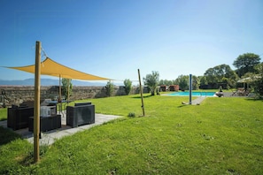 Ein Garten mit Rasen, einem Pool, Gartenmöbeln und einem schattigen Bereich.