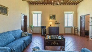 Una sala de estar con un sofá, una mesa con objetos decorativos, una araña y dos ventanas.