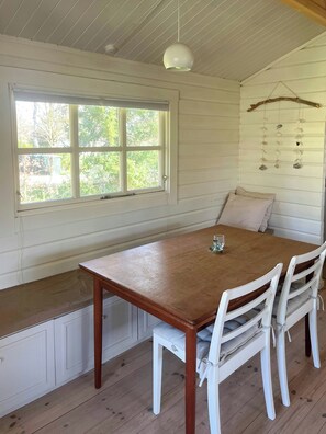 A wooden dining table with chairs, a bench, a hanging light fixture, and a window with a view of greenery. - Family summer house near plantation and beaches (Højby)