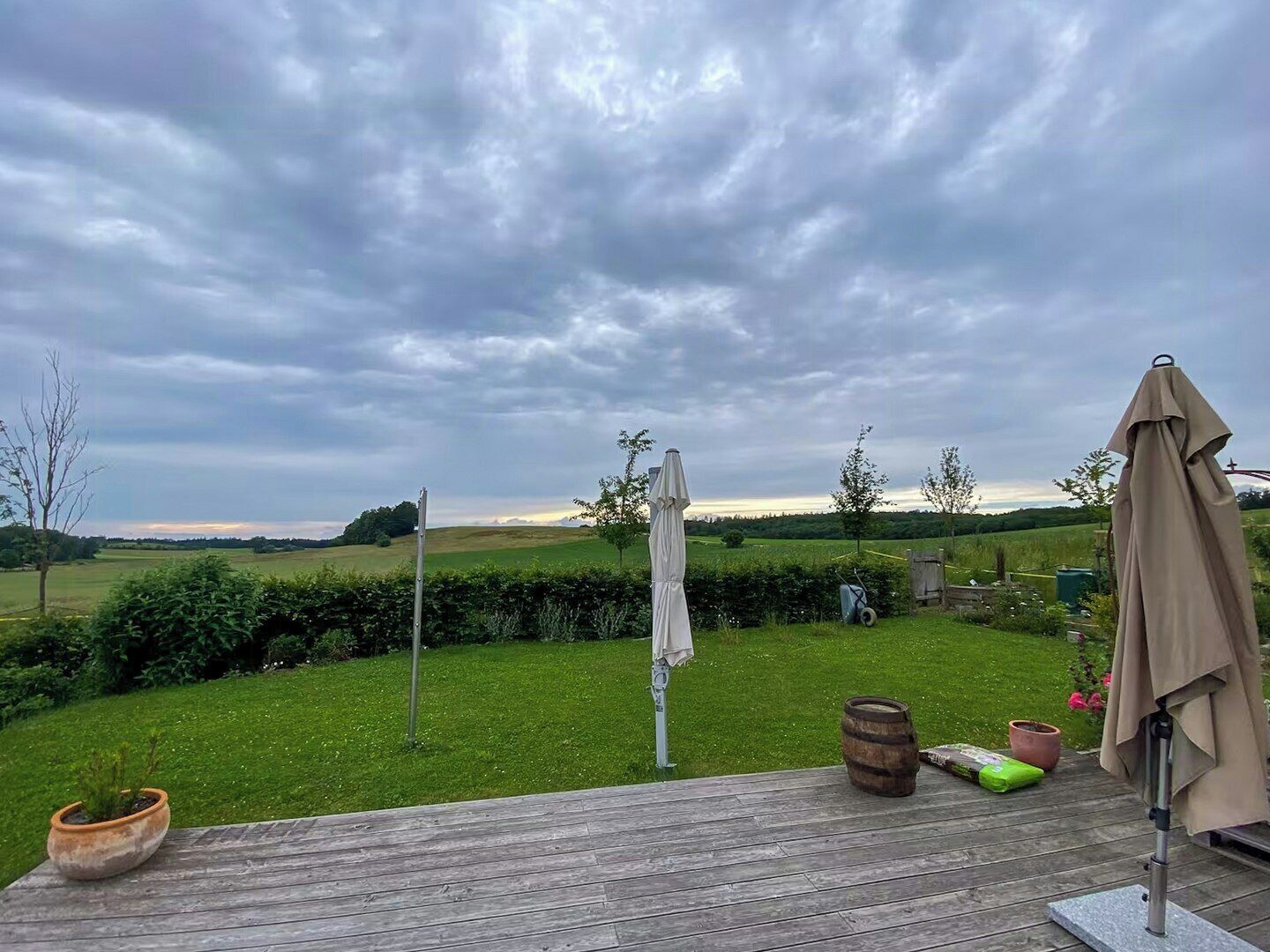 A wooden deck with a view of a grassy field and a cloudy sky.