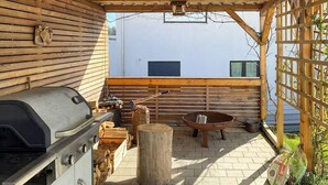 Un patio exterior con una parrilla, un pozo de fuego y una mesa de madera.