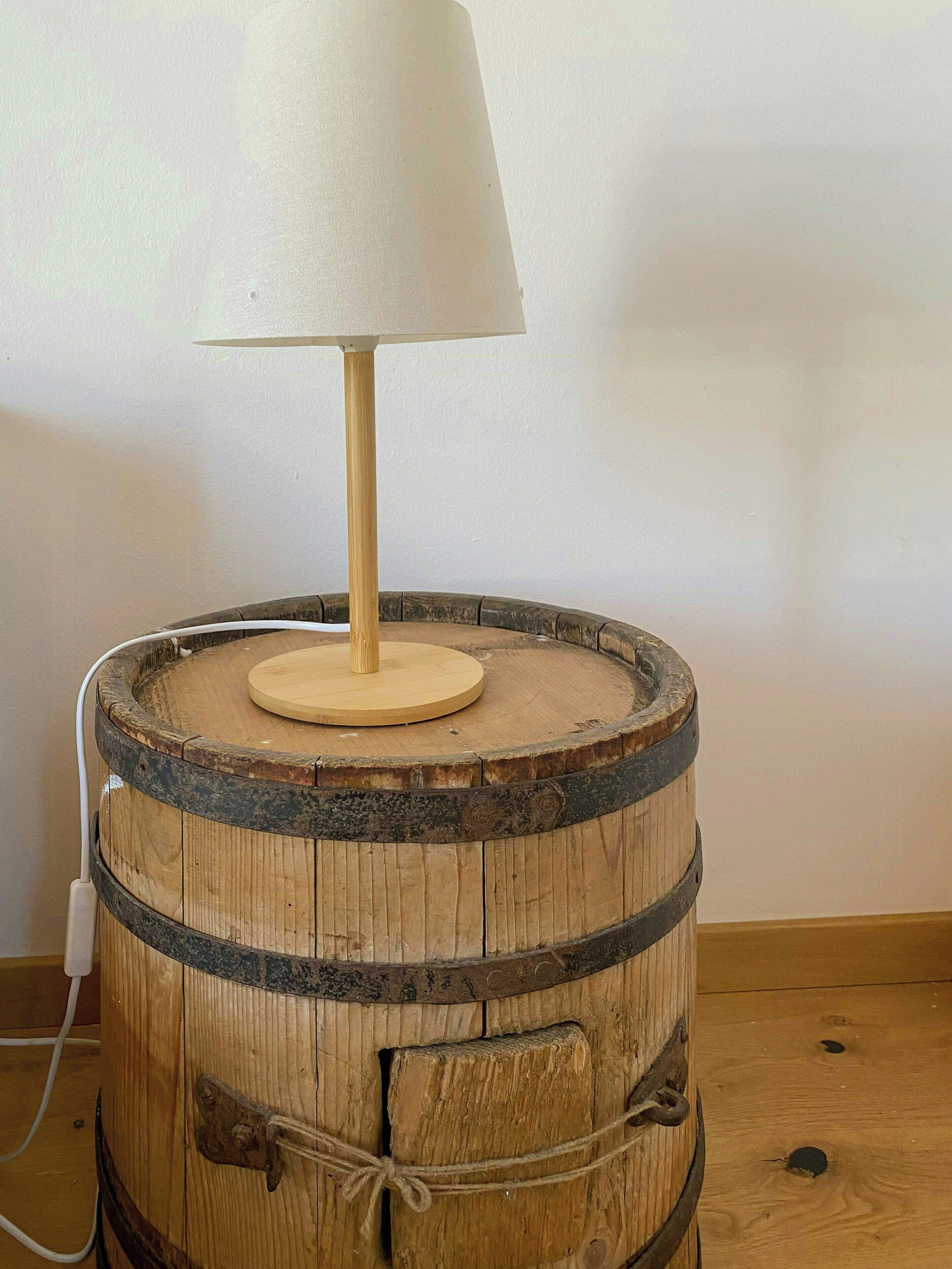 A wooden barrel lamp with a white lampshade on top.