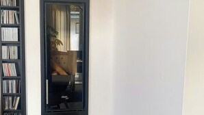 Una habitación con una estantería, un televisor de pantalla plana, una cesta de mimbre con leña y un taburete de madera.
