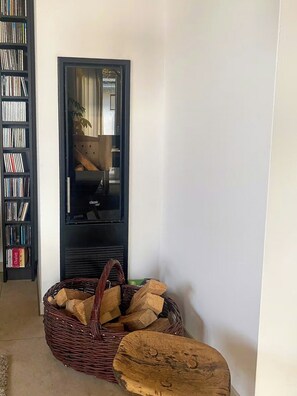 Una habitación con una estantería, un televisor de pantalla plana, una cesta de mimbre con leña y un taburete de madera.
