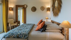 Un dormitorio con cama, almohadas, lámpara, espejo y una silla.