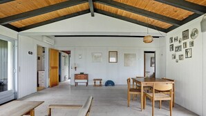 Un intérieur caractérisé par un plafond haut, des poutres en bois, un coin repas avec une table et des chaises, un banc et un mur orné de tableaux encadrés.