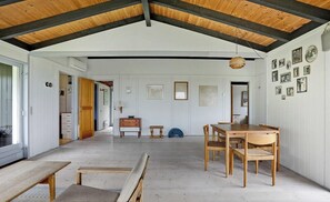 An interior with a high ceiling, wooden beams, a dining area with a table and chairs, a bench, and a wall with framed pictures. - Family house with sea view by Lynæs beach (Hundested)