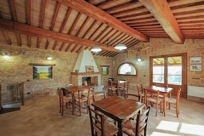 A rustic dining area with wooden tables and chairs, a brick wall, and a fireplace. - Ground floor apartment by Lake Trasimeno (Castiglione del Lago)