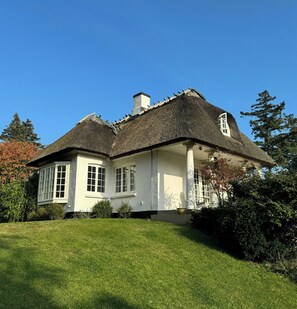 A large house with a thatched roof, white exterior walls, and a well-maintained lawn. - Historic beach villa with pool at Marielyst (Væggerløse)