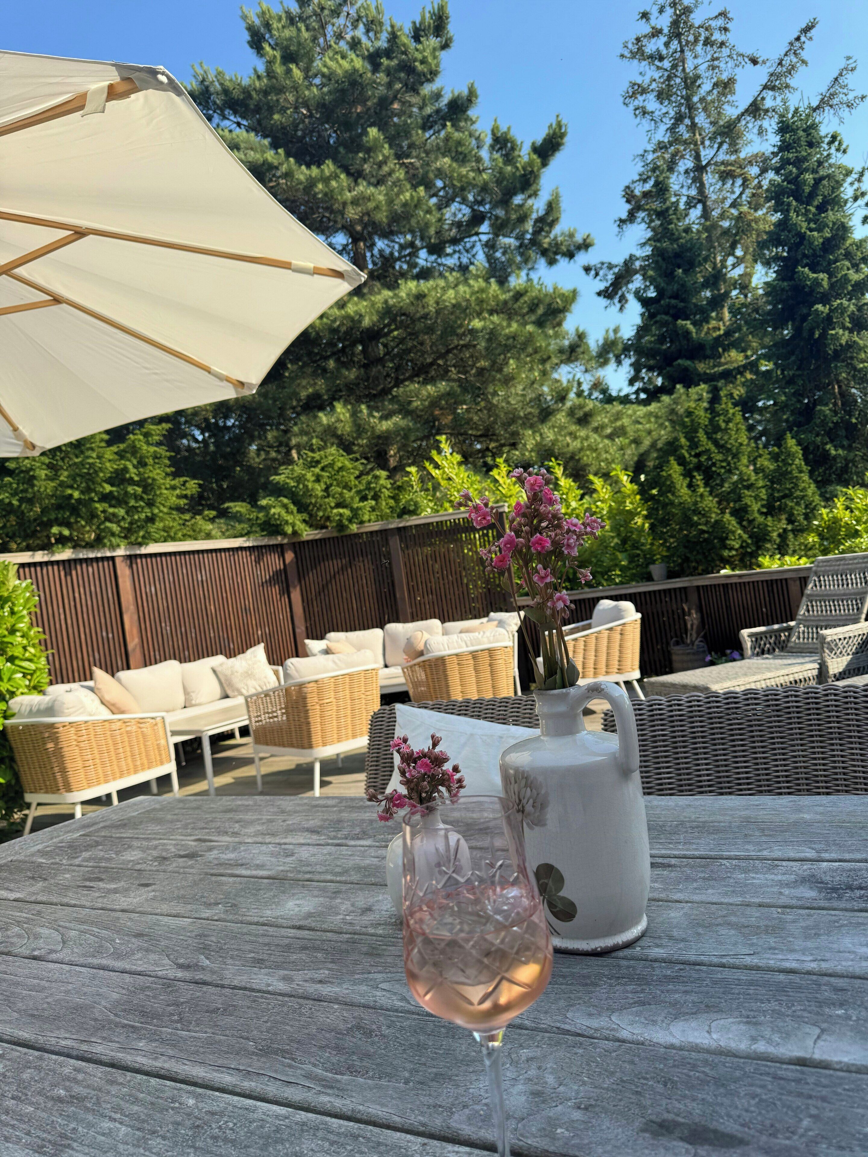 A wooden deck with outdoor furniture, a glass of pink wine, and a vase with flowers.
