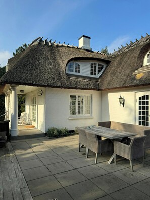 A thatched-roof house with a patio, wicker furniture, and a white exterior. - Historic beach villa with pool at Marielyst (Væggerløse)