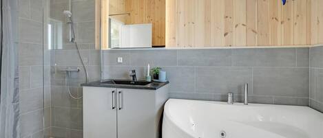 Un bagno moderno con doccia a parete in vetro, una vasca da bagno bianca e un piccolo lavandino con uno specchio sopra.