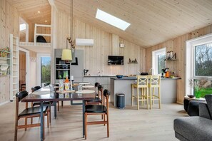 Eine moderne Küche mit einer zentralen Kochinsel, einem Essbereich mit Tisch und Stühlen und einer gemütlichen Sitzecke mit einer Couch.