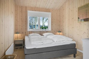 Ein Schlafzimmer mit Doppelbett, Holzwänden, einem Fenster mit Aussicht, Nachttischlampen und einem kleinen Nachttisch.