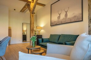 A living room with a green sofa, a blue chair, a small round table with a vase, and a framed picture of deer on the wall. - Relax in a thatched barn with a sauna (Ratekau)
