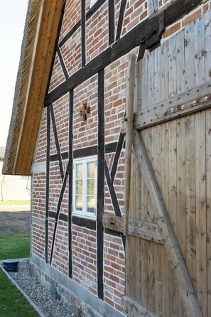 A half-timbered building with exposed brickwork and wooden beams, a wooden door, and a small window. - Relax in a thatched barn with a sauna (Ratekau)