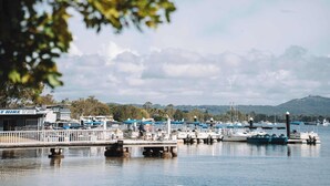 En lystbådehavn med fortøjede både, en mole med et hegn og en bygning med teksten 'AT HIRE' i baggrunden.