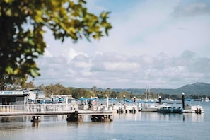 Ein Yachthafen mit vertäuten Booten, eine Pier mit einer Umzäunung und ein Gebäude im Hintergrund, auf dem 'AT HIRE' steht.