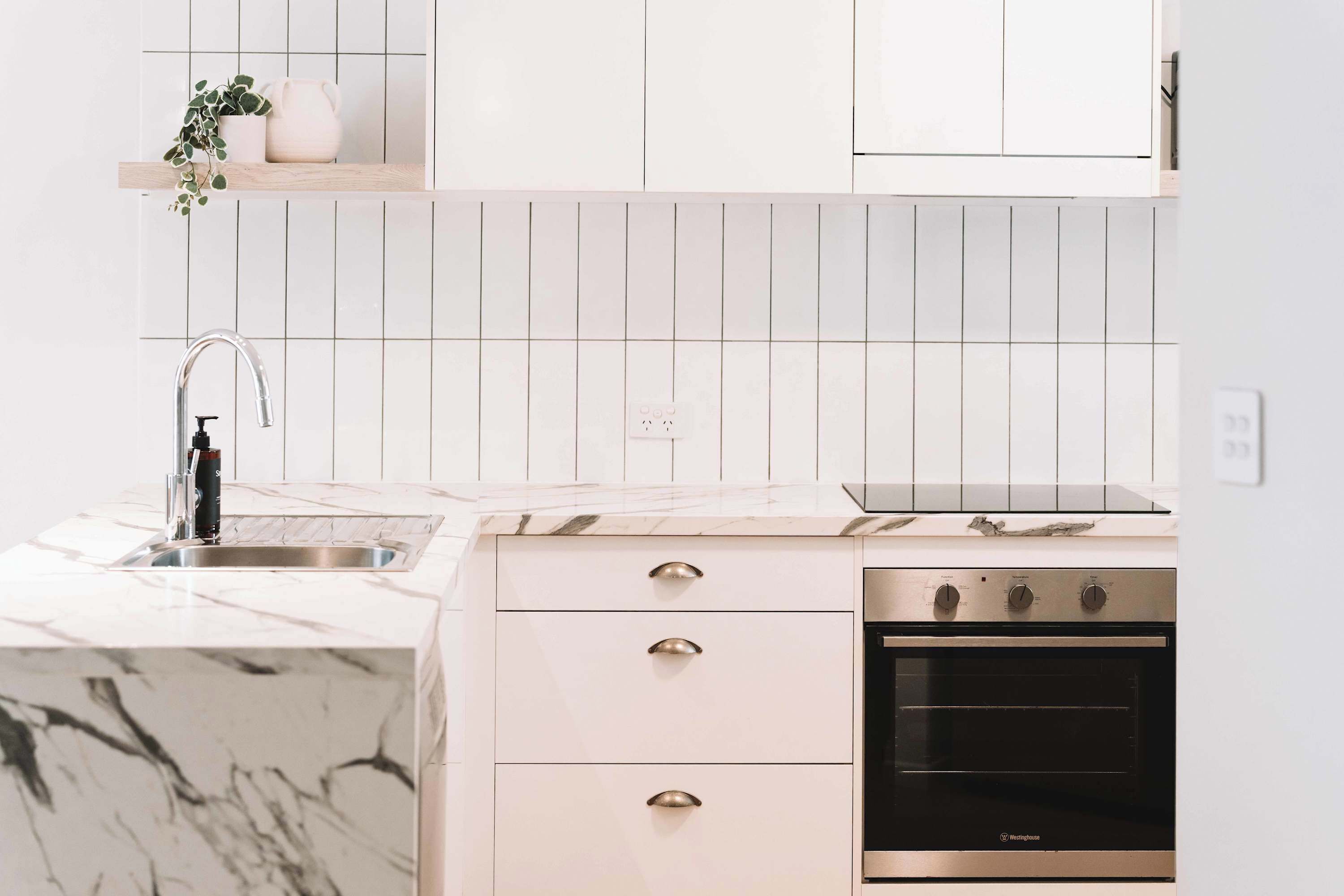Cocina con encimera de mármol, horno de acero inoxidable y muebles blancos.