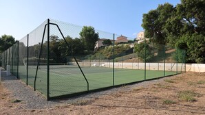 Ein Tennisplatz, umzäunt mit einem Maschendrahtzaun, mit einem Kiesweg davor.