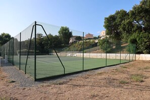 A tennis court enclosed by a chain-link fence with a gravel path in front. - Air-conditioned villa with shared pool 4+2 near beaches (LES ISSAMBRES)