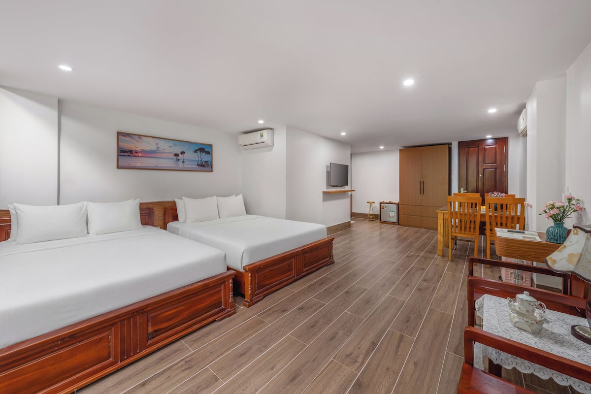 Quarto de hotel com duas camas, televisão, pintura e área de refeições com cadeiras e mesa.