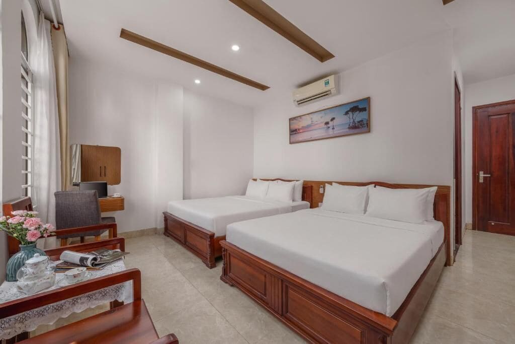 A hotel room with two beds, a desk with a chair, a TV, and a painting on the wall.
