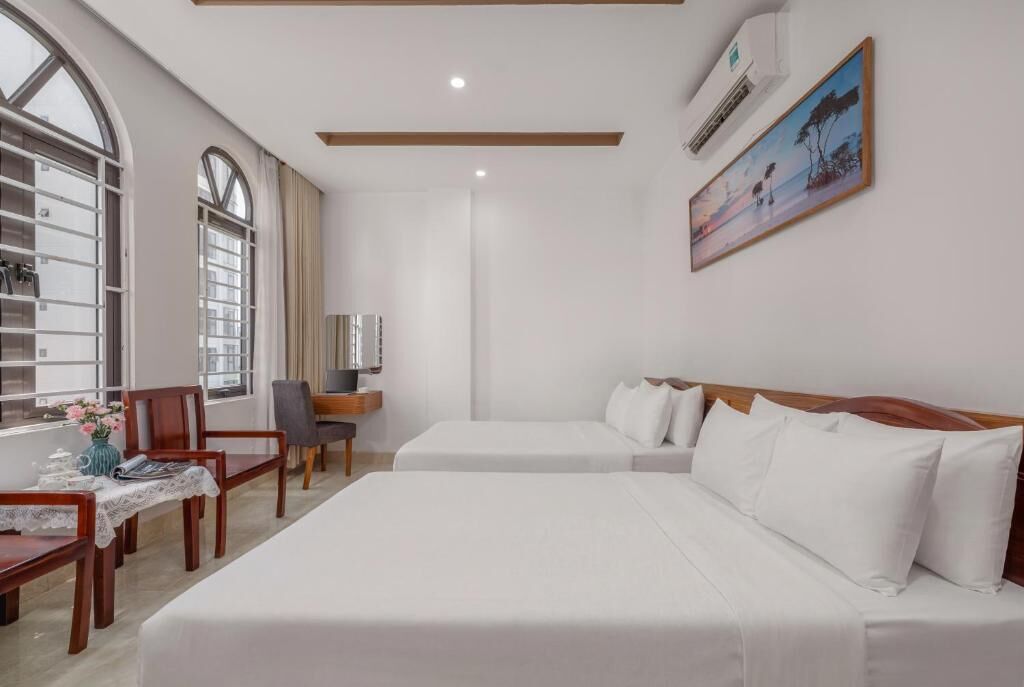 A hotel room with two beds, a desk, a chair, a window with curtains, and a painting on the wall.