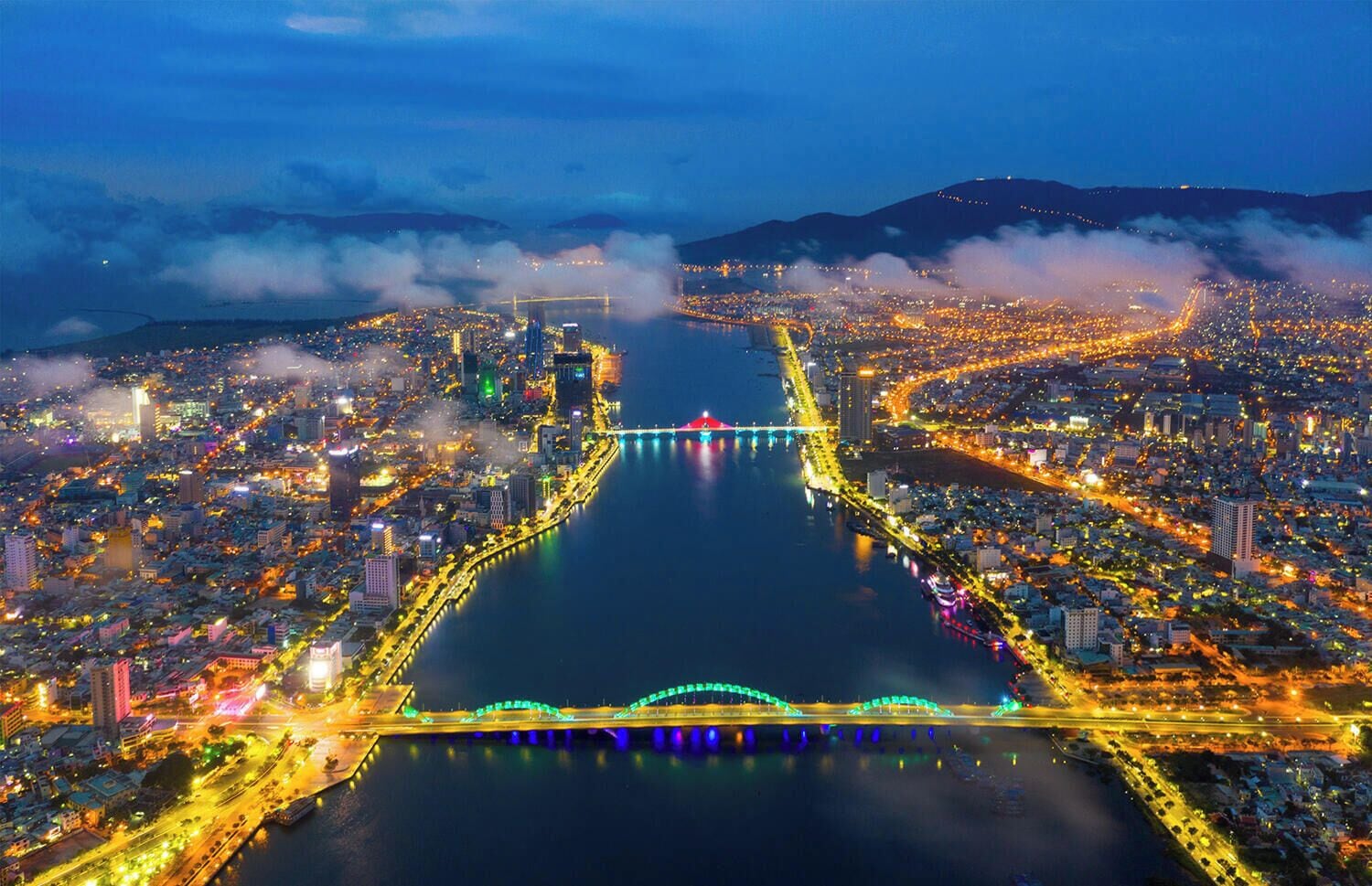 A nighttime aerial view of a city with a prominent river, bridges, and dense urban lighting.
